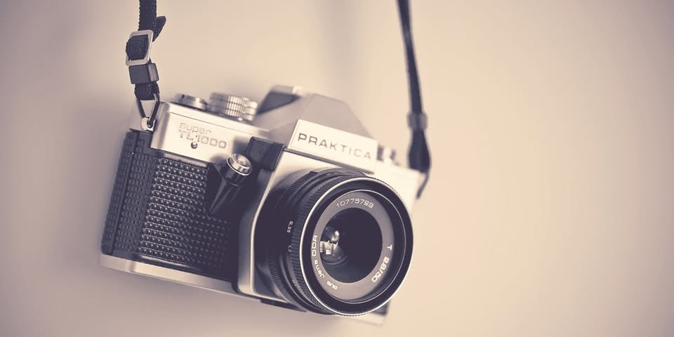 Close-up of a vintage film camera with a lens and black strap.