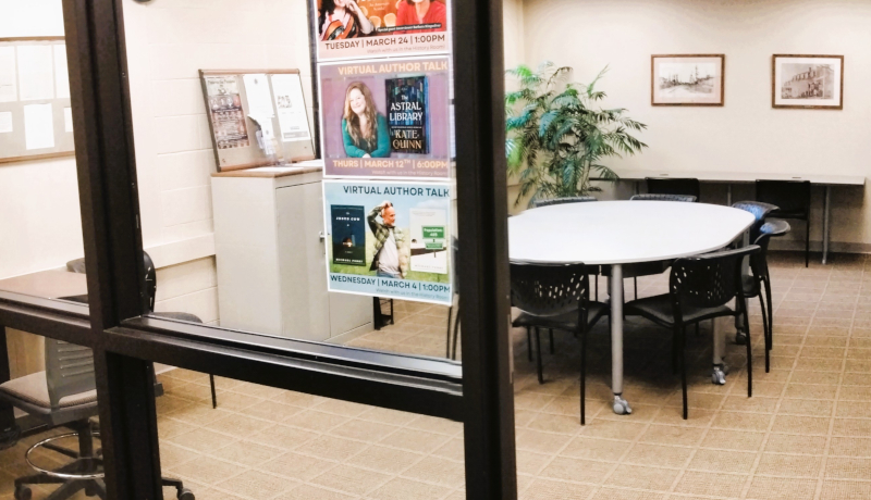 History room. A small meeting room with a circular table, chairs, and posters on the glass wall.
