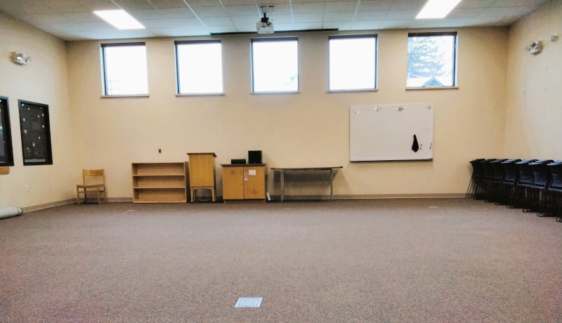 Program Room. Empty room with windows, a whiteboard, and stacked chairs.