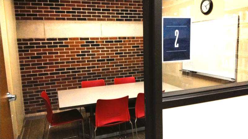 Study room 2. A study room with a table, red chairs, a brick wall, a whiteboard, and a sign with the number "2".