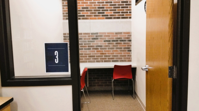 Study room 3. A small study room with a table, a red chair, and a brick wall and the number "3". A door is partially open.